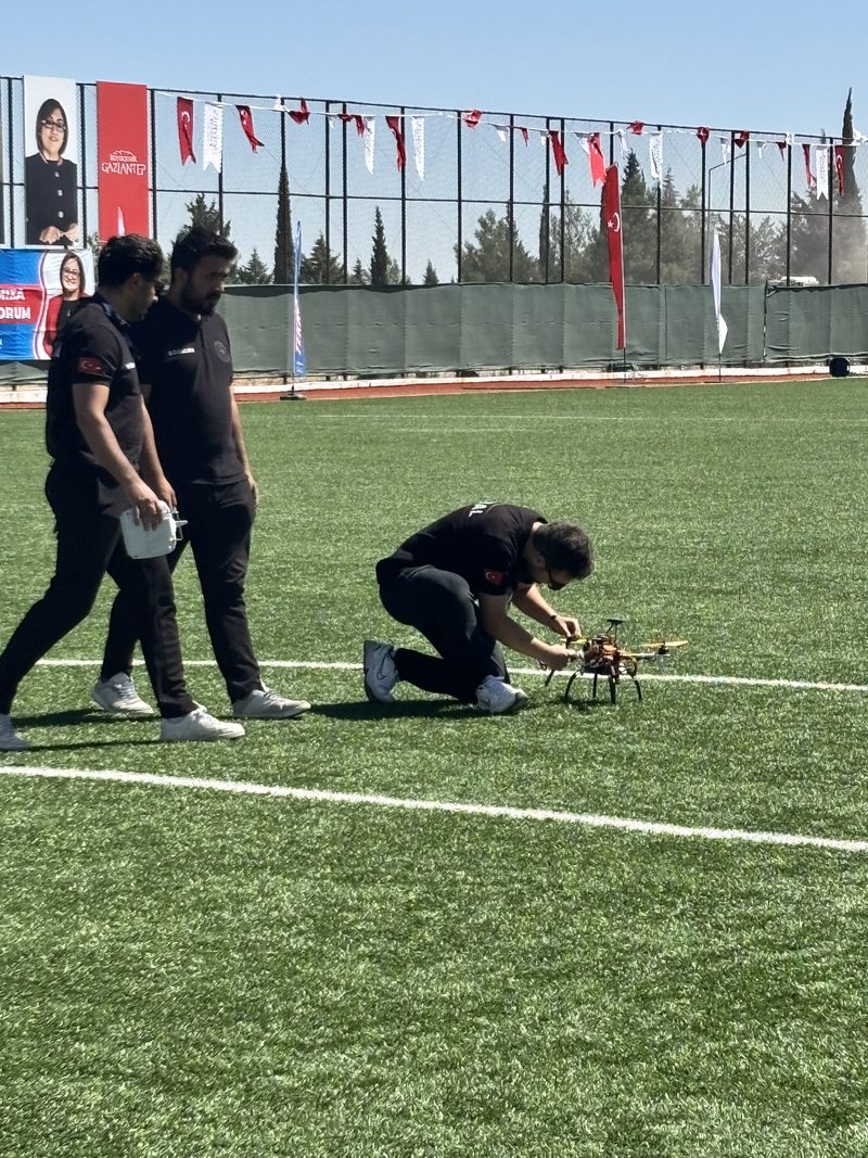 İstikbal tişörtlü iki takım üyesi sahada İHA'ya doğru yürüyor